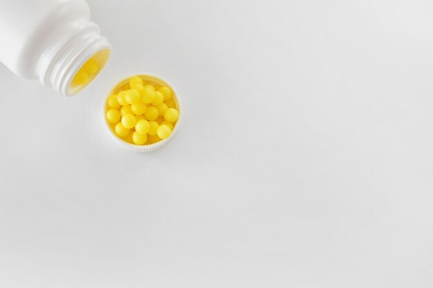 Gele vitamines in de vorm van ronde dragees gieten uit een pot op een lichte achtergrond vitamine C