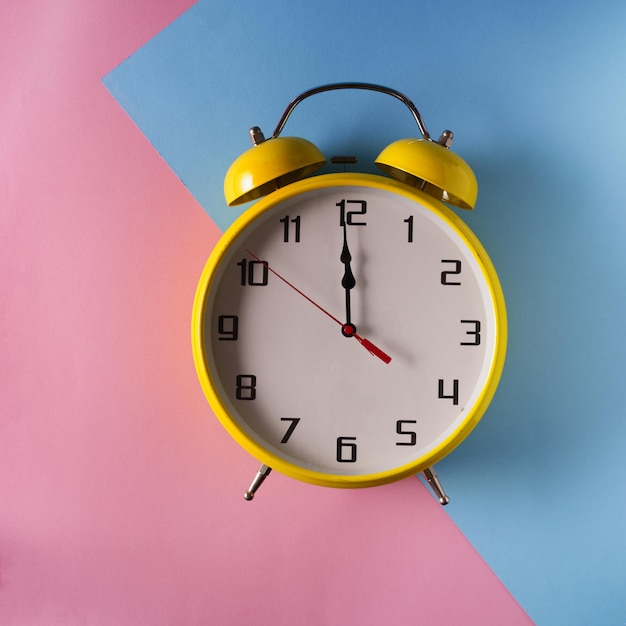 Gele wekker in retro stijl op roze en blauwe achtergrond