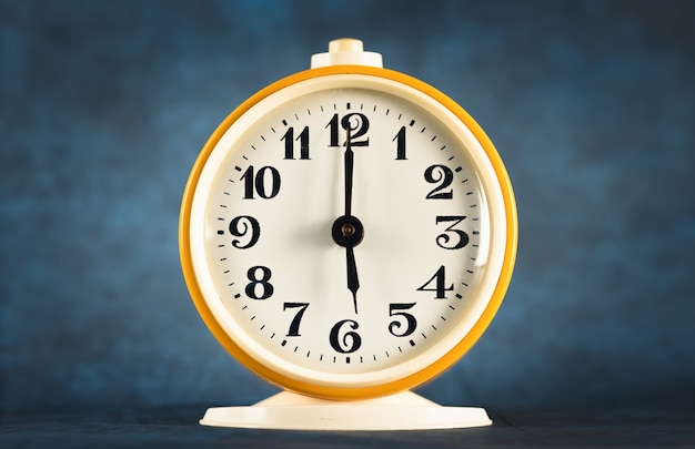 Gele wekker toont de tijd 18 uur op een donkere geïsoleerde achtergrond