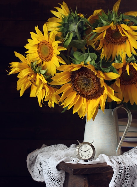 Gele zonnebloemen in een kruik en een klok. retro stilleven met een boeket van tuinbloemen.