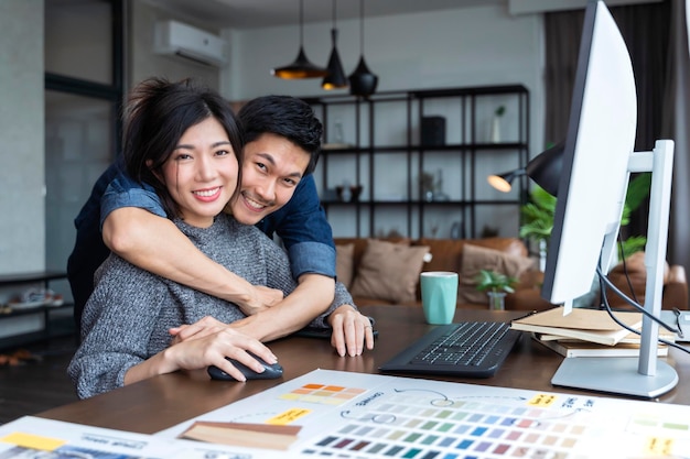 Geluk aziatische mensen paar thuis werken met vrolijk en geluk knuffelen samen met liefde en joyfulasian trouwen paar werken met computer in woonkamer thuis met knuffel ondersteuning echtgenoot