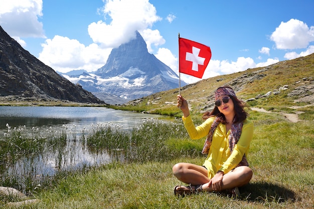 Geluk Aziatische vrouw zitten en glimlachen met Zwitserse vlag in de buurt van het alpine meer van Riffelhorn
