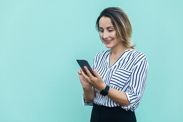 Geluk en mooie zakenvrouw die in de buurt van een lichtblauwe muur staat en smartphone gebruikt