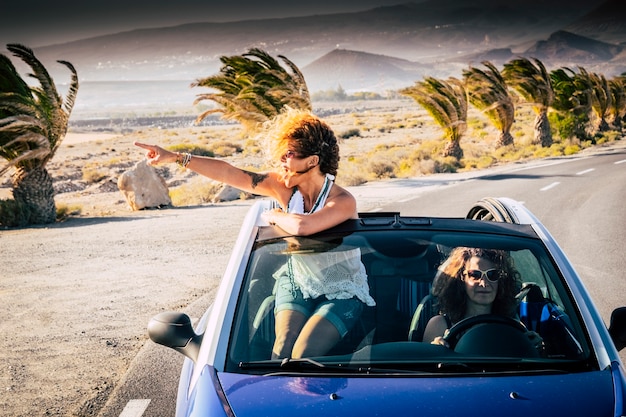 Geluk en reizen levensstijl mensen - paar vrouwelijke volwassenen vrienden rijden en reizen op een blauwe cabriolet - uit het dak mooie krullende blonde vrouw kijken en genieten van de reis