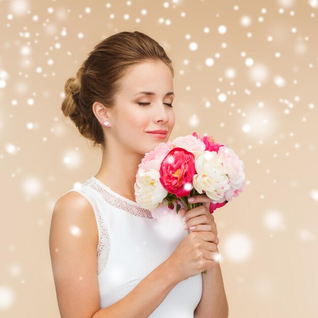 geluk, huwelijk, vakantie en viering concept - lachende bruid of bruidsmeisje in witte jurk met boeket bloemen over beige achtergrond en sneeuw