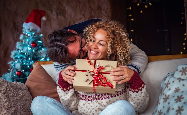 Geluk in het seizoen van de kerstvakantie vooravond Man doet een verrassing aan gelukkige vrouw die haar een kerstcadeau geeft in een rode versierde doos kerstboom op de achtergrond Paar vieren samen met liefde vreugde