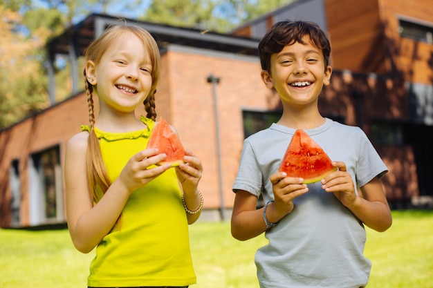 Geluk in ons. Vrolijke charmante kinderen glimlachen en eten een rijpe watermeloen