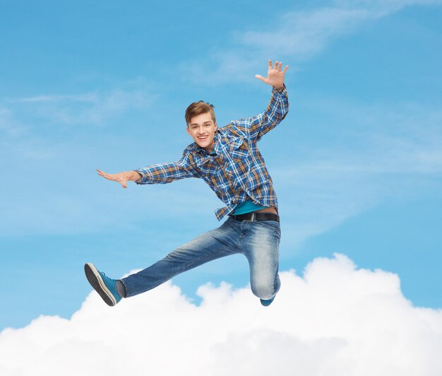 geluk, vrijheid, beweging en mensenconcept - glimlachende jonge mens die in lucht over blauwe hemel met witte wolkenachtergrond springt