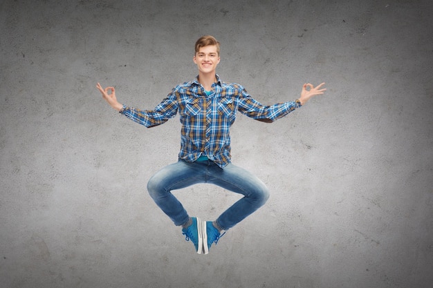 geluk, vrijheid, beweging en mensenconcept - glimlachende jonge mens die in lucht over concrete muurachtergrond springt