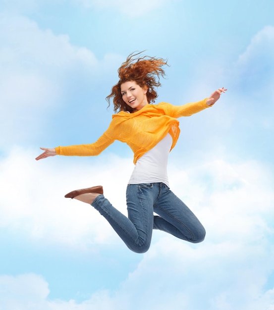 geluk, vrijheid, beweging en mensenconcept - glimlachende jonge vrouw die hoog in de lucht springt over blauwe hemel met wolkenachtergrond