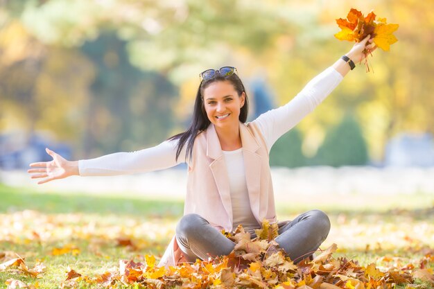 Geluk vrouw zitten in herfst park met boeket met herfstbladeren.