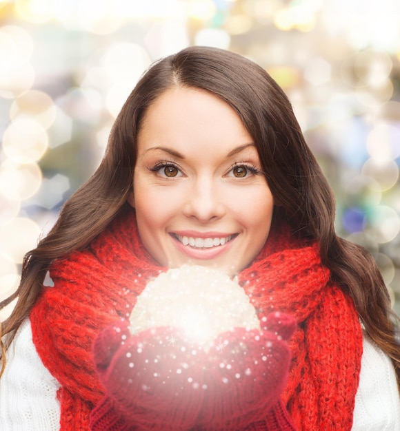 Foto geluk, wintervakantie en mensenconcept - glimlachende jonge vrouw in rode sjaal en wanten met kerstbal over lichtenachtergrond