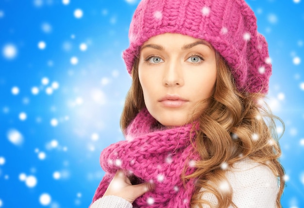 geluk, wintervakantie, kerstmis en mensenconcept - close-up van jonge vrouw in roze muts en sjaal over blauwe besneeuwde achtergrond