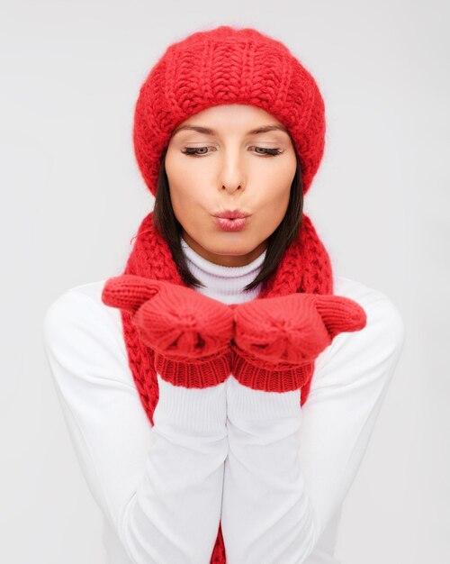 geluk, wintervakantie, kerstmis en mensenconcept - glimlachende jonge vrouw in rode muts, sjaal en wanten over grijze achtergrond