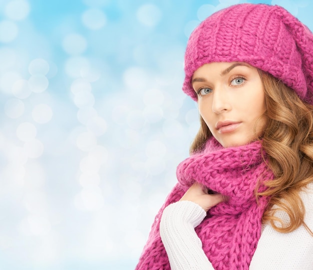 geluk, wintervakantie, kerstmis en mensenconcept - jonge vrouw in roze hoed en sjaal over blauwe lichtenachtergrond
