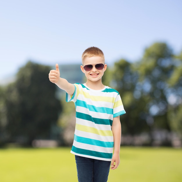 geluk, zomer, jeugd, gebaar en mensen concept - lachende schattige kleine jongen in zonnebril over park achtergrond duimen opdagen