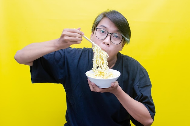 Gelukkig aantrekkelijke aziatische man met peek a boo haar eet hongerig noedels op kom met eetstokje