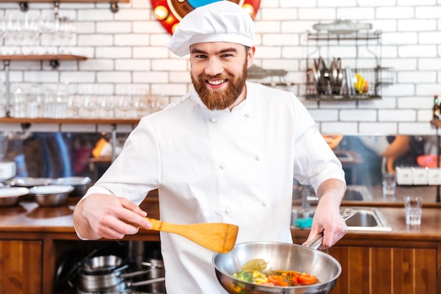 Gelukkig aantrekkelijke chef-kok koken met koekenpan op de keuken