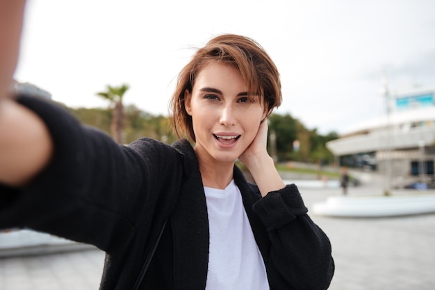 Foto gelukkig aantrekkelijke jonge vrouw die selfie buitenshuis