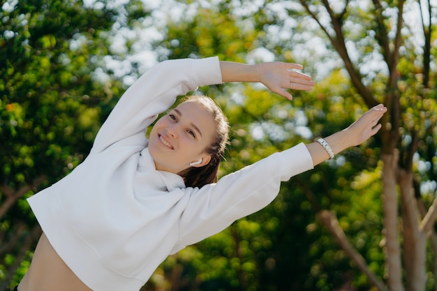 Gelukkig actieve jonge vrouw strekt armen leunt opzij glimlacht positief geniet van sporten