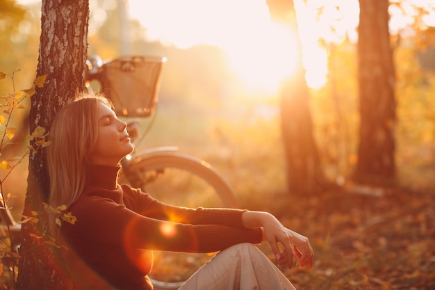 Gelukkig actieve jonge vrouw zitten met vintage fiets in herfst park bij zonsondergang