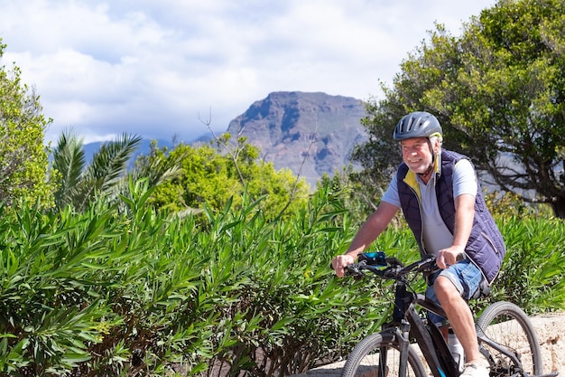 Gelukkig actieve senior man met elektrofietsen die buiten in het park staan Glimlachende bejaarde grootvader die in de natuur loopt met zijn fiets en geniet van een gezonde levensstijl