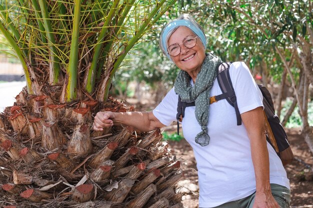 Gelukkig actieve senior vrouw met rugzak in openlucht excursie genieten van gezonde levensstijl en zonnige dag Oudere aantrekkelijke vrouw in tropische bossen glimlacht camera kijken
