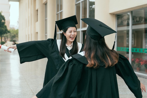 Gelukkig afgestudeerde jonge multi-etnische studenten knuffelen. mooie slimme universiteitsstudent klaar met school zorg liefde emotie naar vriend klasgenoot glimlachen lachen open armen handen uit gebouw