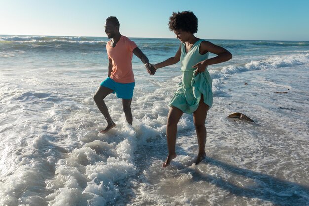 Gelukkig afrikaans amerikaans paar genieten van zomervakantie waden aan de kust op het strand tijdens zonnige dag