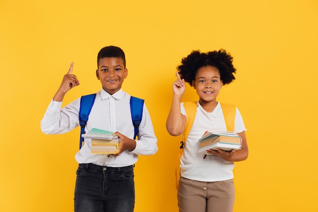 Gelukkig afrikaans amerikaans schoolmeisje en gemengd ras schooljongen samen op gele achtergrond kopie ruimte