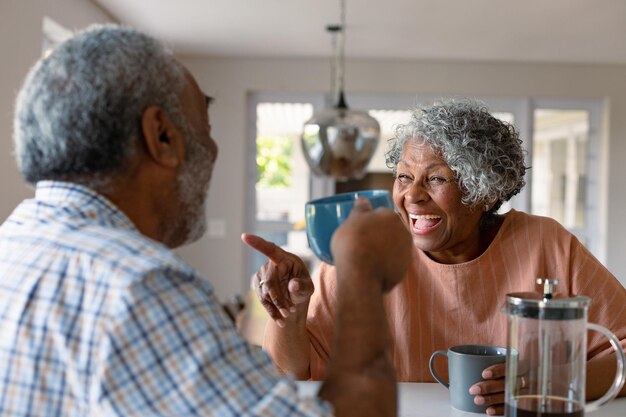 Gelukkig Afrikaans Amerikaans senior koppel zit in de keuken met koffie en praat