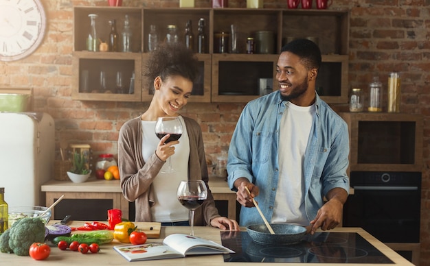 Gelukkig Afrikaans-Amerikaans stel dat samen diner kookt en rode wijn drinkt