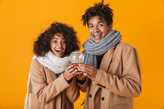 Gelukkig Afrikaans paar dat de winterkleren draagt die zich geïsoleerd bevinden, sneeuwbol houden