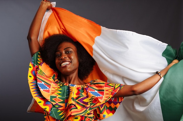 Foto gelukkig afrikaanse vrouw in nationale kleding glimlachend en poseren met een vlag ivoorkust c te d'ivoire geïsoleerd over een grijze achtergrond