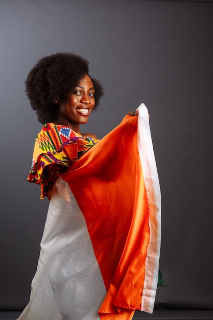 Gelukkig afrikaanse vrouw in nationale kleding glimlachend en poseren met een vlag ivoorkust c te d'ivoire geïsoleerd over een grijze achtergrond