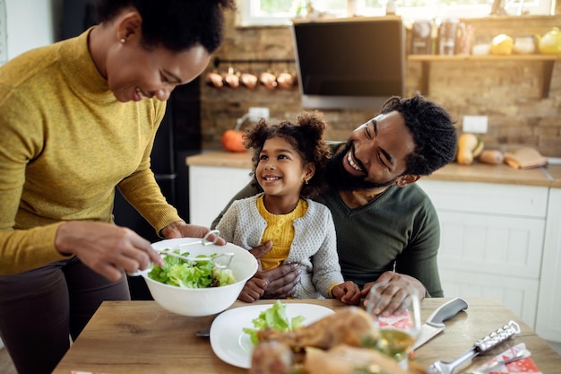 Gelukkig Afro-Amerikaans meisje met Thanksgiving-lunch met haar ouders aan de eettafel