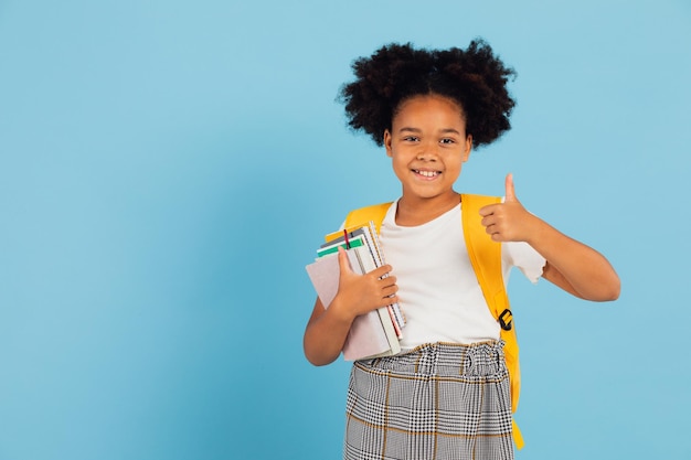 Gelukkig Afro-Amerikaans schoolmeisje dat cool op blauwe achtergrond wijst terug naar schoolconcept