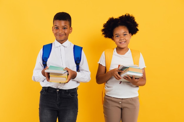 Gelukkig Afro-Amerikaans schoolmeisje en gemengd ras schooljongen met boeken op gele achtergrond kopie ruimte