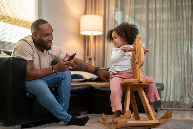 Gelukkig Afro-Amerikaanse man speelt met zijn dochter in de woonkamer thuis