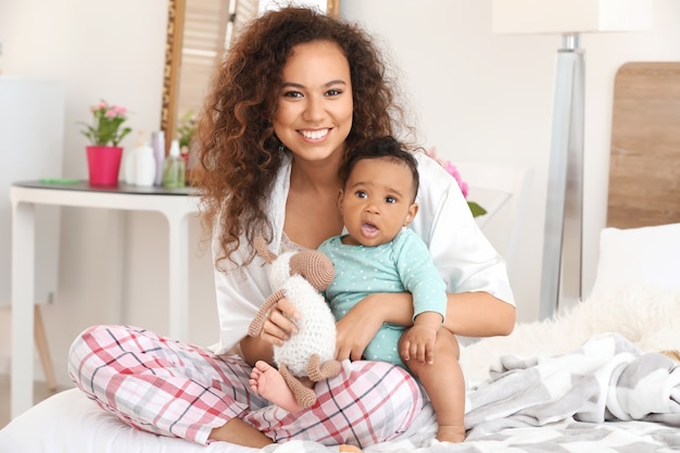 Gelukkig Afro-Amerikaanse moeder met schattige kleine baby in de slaapkamer