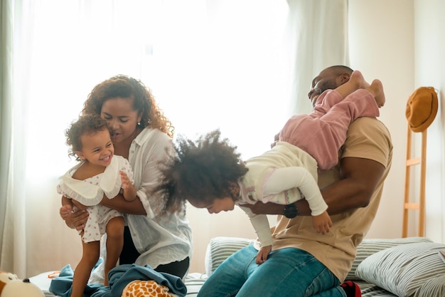 Gelukkig Afro-Amerikaanse ouders met kleine dochters spelen op het bed in de slaapkamer thuis