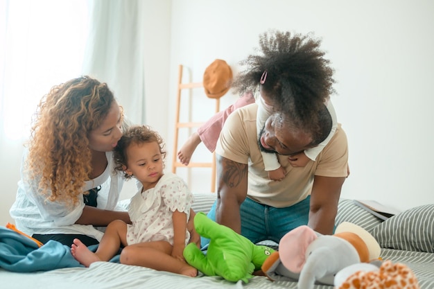 Gelukkig Afro-Amerikaanse ouders met kleine dochters spelen op het bed in de slaapkamer thuis