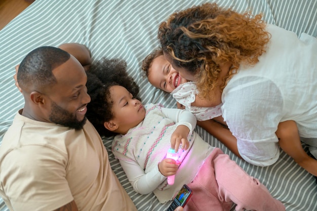 Gelukkig Afro-Amerikaanse ouders met kleine dochters spelen op het bed in de slaapkamer thuis