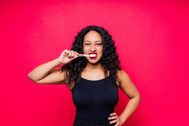 Gelukkig afro-amerikaanse vrouw borstelt tanden mondhygiëne concept geïsoleerd op rode achtergrond