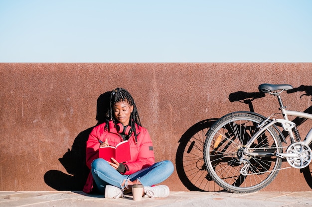 Gelukkig Afro-Amerikaanse vrouw met fiets zittend op straat en schrijven in een notitieboekje