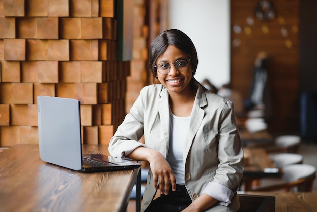 Gelukkig Afro-Amerikaanse vrouw werknemer met behulp van laptop werk studie op computer in loft kantoor of café, glimlachend gemengd ras vrouwelijke student freelancer met behulp van pc-app dating communiceren online kijken webinar