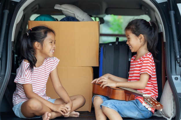 Gelukkig Aziatisch kind meisje gitaar spelen en zingen een lied met haar zus in een auto kofferbak