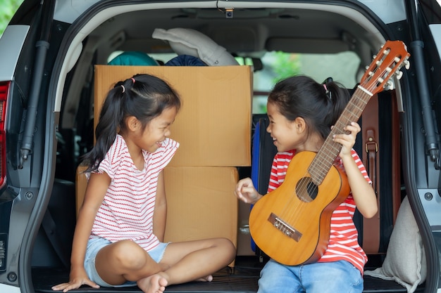 Gelukkig aziatisch kind meisje gitaar spelen en zingen een lied met haar zus in een auto kofferbak