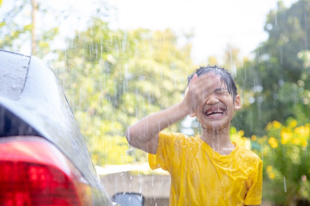 Gelukkig Aziatisch meisje dat auto wast op waterspatten en zonlicht thuis