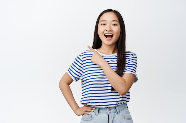 Gelukkig Aziatisch meisje lacht en glimlacht toont advertentie wijst vinger in de linkerbovenhoek bij verkoop banner beveelt winkelstands op witte achtergrond aan